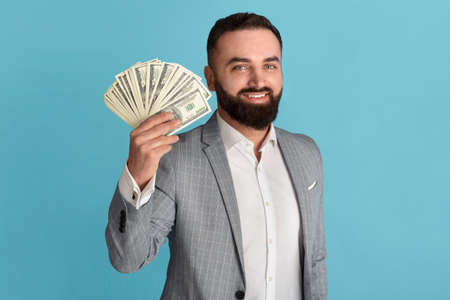 Happy businessman holding fan of American money against blue backgroundの写真素材