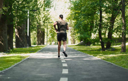 Back view of black sportsman running at beautiful green park in morning, panoramaの写真素材