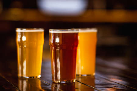 Beer craft style. Barley, unfiltered, light drink in glasses on wooden table in blurry interior of pubの写真素材