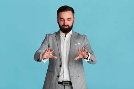 Serious young entrepreneur touching interactive virtual screen against blue background, space for designの写真素材