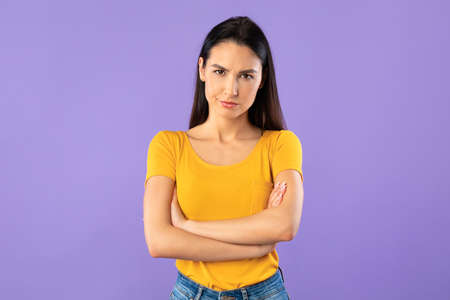 Conflict Concept. Angry girl with crossed arms and pursed lips looking at camera over purple studio wall, copyspaceの写真素材