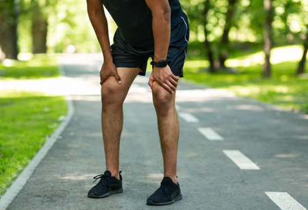 Unrecognizable millennial jogger resting during his morning run at summer park, closeup of legsの写真素材