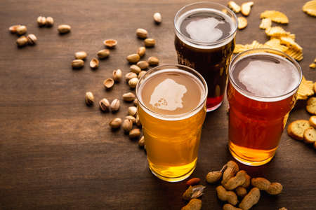 Different craft beer for every clients. Snacks are scattered on brown wooden table, close up, free spaceの写真素材