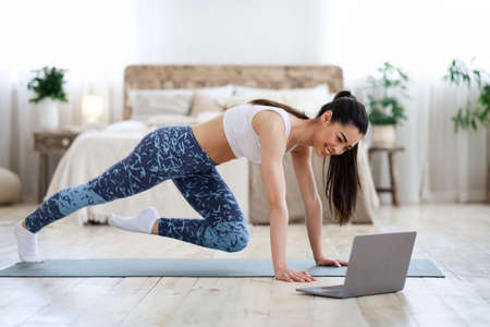 Home Workout. Young Asian Girl Practicing Sport In Front Of Laptop, Doing Leg Exercises In Living Room, Free Spaceの写真素材