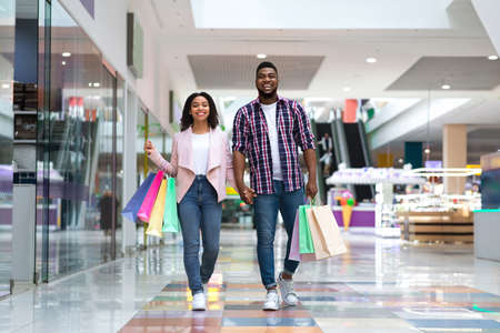 Shopping Concept. Happy Black Couple Walking In Mall Carrying Colorful Shopper Bags, Free Spaceの写真素材