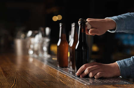 Evening with company in pub. Barman opens beer bottles on wooden bar counter in interior, free space
