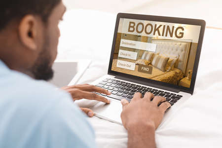 African american man browsing hotel booking web service online, using laptopの写真素材