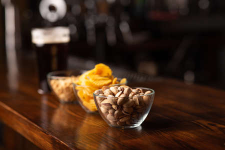 Snack to beer. Pistachios, chips and peanut in glass bowls on wooden brown bar counter, free spaceの写真素材
