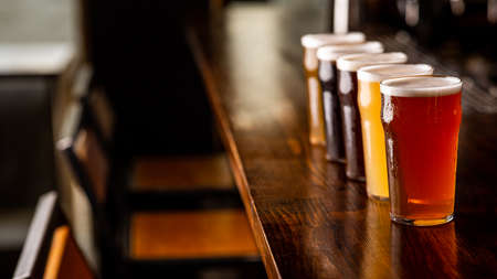 Party with friends in pub. Row of glasses of beer of different sorts on wooden bar counter in...