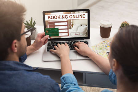 Back view of couple making hotel reservation online, using laptop and credit card, hotel booking website conceptの写真素材