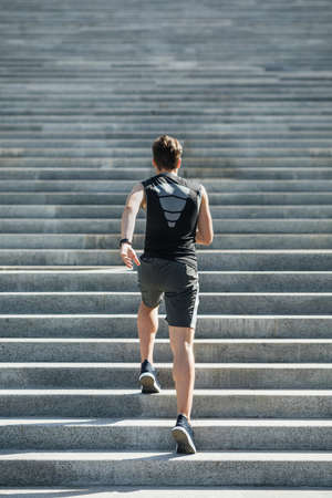 Running up stairs. Young man in sportswear and with fitness tracker on hand, goes in for sport in...