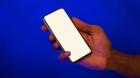 Male Hand Holding Cellphone With Empty Screen For Your Text Advertising Mobile Application On Blue...