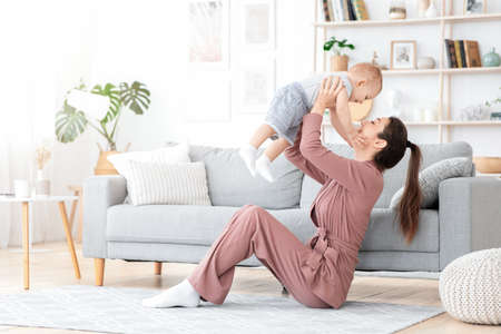 Unconditional Love. Happy young mom enjoying time with her toddler son at home, lifting him in the...