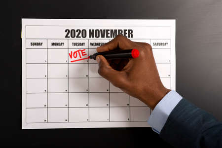 African american businessman writing Vote on November 3, 2020, presidential elections, patriotic conceptの写真素材
