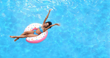 Excited young woman enjoying summer sun on inflatable ring at pool, above view. Empty space....