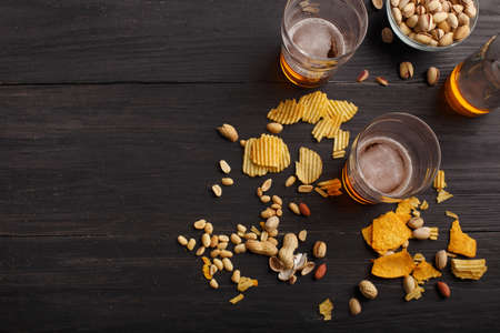 Drinks for two. Glasses with light beer stand on dark wooden table, near are bottle and pistachios in glass plate, top viewの写真素材