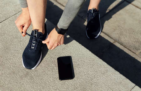 Start of training. Athlete tying shoelaces on sneakers, telephone on steps near, cropped, close up,...