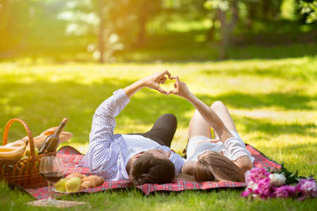 Loving couple making heart with hands during picnic at park in summertimeの写真素材