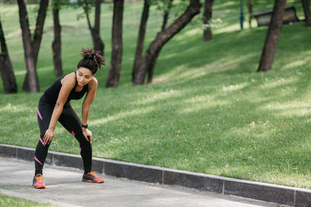 Take a breath while jogging. Tired african american girl in sportswear with fitness tracker and...