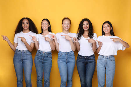 Look There. Five Multiracial Women Pointing Fingers Aside Advertising Something Standing Over Yellow...