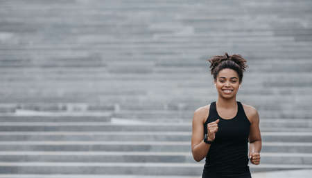 Run of stairs in city. Smiling african american girl with wireless headphones and smart watch, free spaceの写真素材