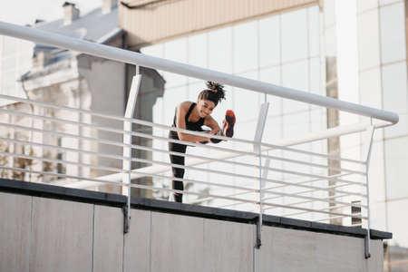 Legs warming and stretching. African american girl in fashion sportswear, doing exercises at stadium, free spaceの写真素材