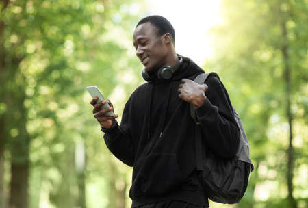 Happy african guy using smartphone, sharing his sport achievements, training at parkの写真素材