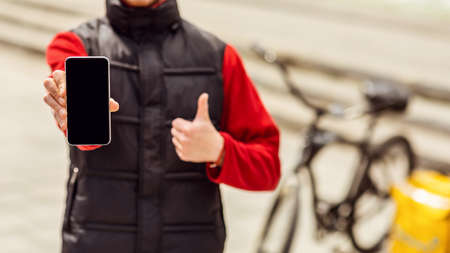 Courier Showing Mobile Phone Empty Screen Delivering Food On Bicycle Outdoors. Online Delivery App...