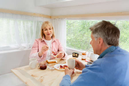 Happy married couple having toasts with jam for breakfast inside motorhome during camping tripの写真素材