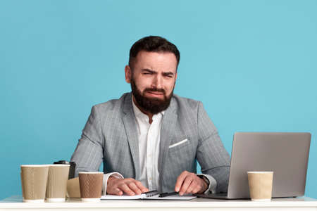 Young office employee whining or crying at desk because of too much work, blue backgroundの写真素材