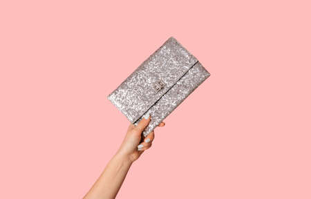 Young woman showing silver sparkly clutch bag on pink background, closeup of handの写真素材