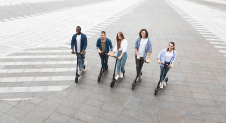 Eco Friendly Transport. Five cheerful smiling multicultural friends riding e-scooters, high angle viewの写真素材