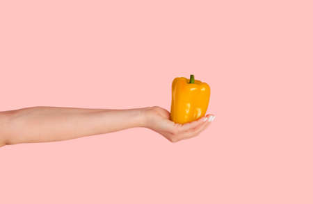 Millennial woman holding yellow bell pepper over pink background, closeup view