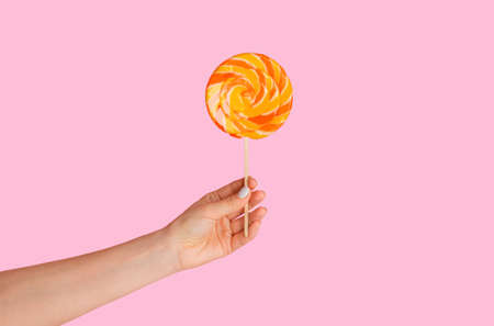 Millennial girl holding yummy swirl lollipop over pink background, close up of handの写真素材