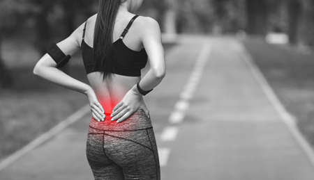 Lower Back Ache. Female athlete rubbing hurt back with painful injury, touching inflamed zone, black and white image with red sore spot, panoramaの写真素材
