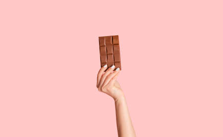 Millennial woman holding bar of organic chocolate over pink background, close up of hand. Panoramaの写真素材