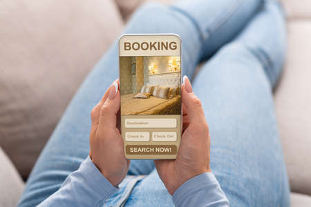 Girl getting ready for journey, choosing hotel on mobile app, using smartphone at home, croppedの写真素材