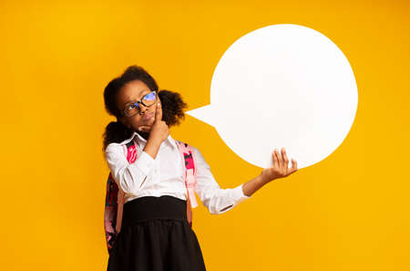 Pensive Black Schoolgirl Posing With Speech Bubble Thinking Of School On Yellow Background. Mockup, Studio Shotの写真素材