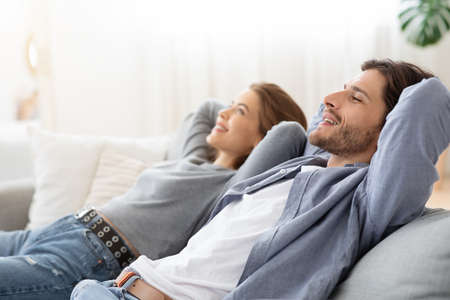 Side view of young chilling couple enjoying day off at home. sitting on soga at living room, copy spaceの写真素材