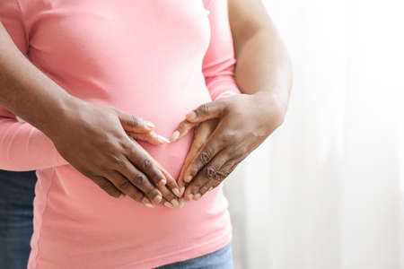 Closeup of unrecognizable african pregnant couple placing hands on top of each other in heart shape...