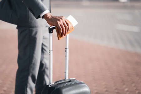 Business Trip. Unrecognizable Businessman Holding Passport And Boarding Pass Standing With Travel Suitcase Outdoor At Airport. Closeup, Cropped, Copy Spaceの写真素材