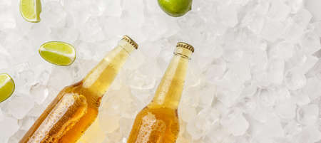 Chilled drink for summer heat. Two cold glass bottles with light beer without labels in ice with pieces of lime, panorama, free spaceの写真素材