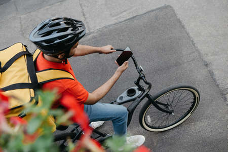 Find address. Bicycle courier in protective helmet with delivery backpack sits on bicycle and looks...