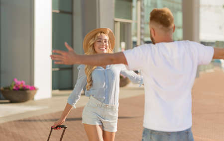 Happy guy meeting his girl after arrival standing with open arms near airport building