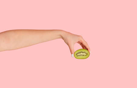 Female hand holding cut kiwi fruit against pink background, closeup viewの写真素材