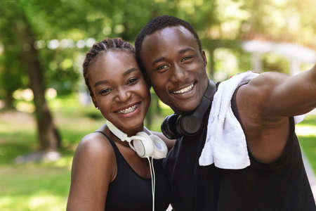 Happy black fitness couple taking selfie after jogging outdoors, posing in summer city park after trainingの写真素材