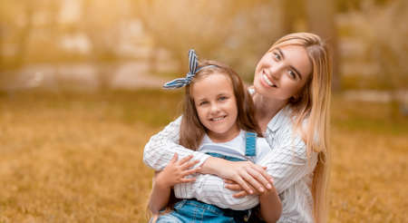 Young Mother Hugging Little Daughter Smiling To Camera Sitting In Park Outdoor In Autumn. Free Space...