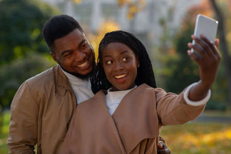 Two african american lovers taking romantic selfie with smartphone outdoors, selective focus on coupleの写真素材