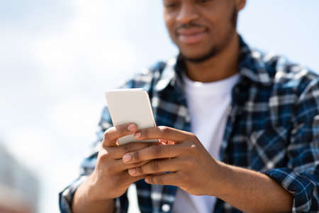 Closeup of confident african american person holding cell phone and textingの写真素材