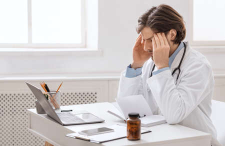 Overworked male doctor suffering from headache at workplace, empty spaceの写真素材
